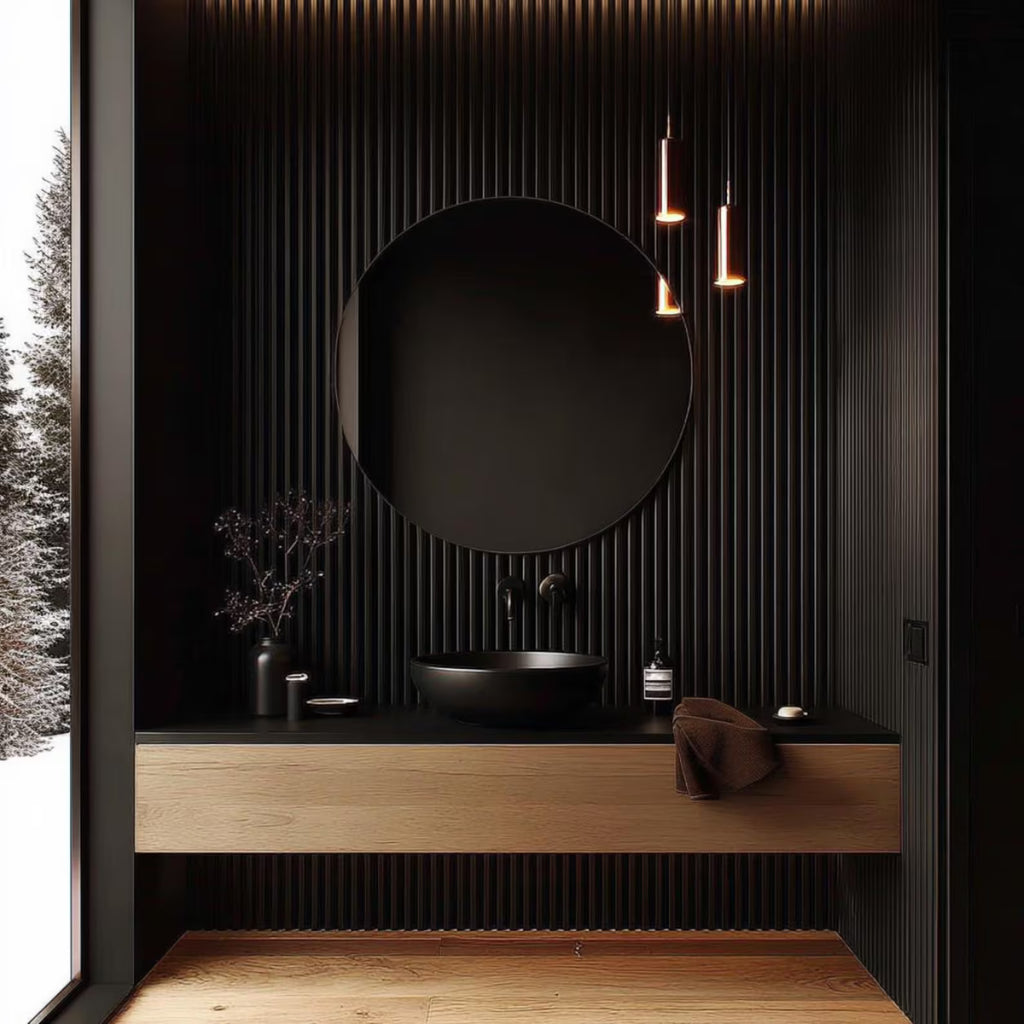 A modern bathroom vanity with a black round vessel sink, matte black round mirror, and floating light wood vanity cabinet against a black ribbed wall. A large window on the left shows a snowy outdoor scene, and three hanging pendant lights illuminate the space.